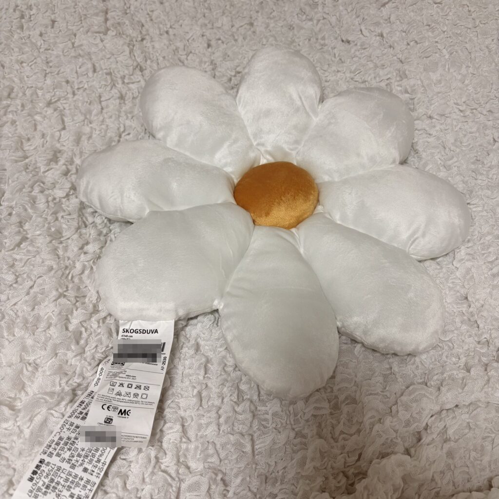 IKEAのデイジー形クッションSKOGSDUVA。白い花びらに黄色いまん中、タグ付き
