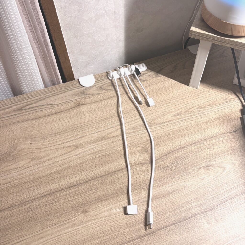机の奥のふちに貼った白いケーブルホルダー。充電ケーブルが並んで、机の手前にまっすぐ垂れている