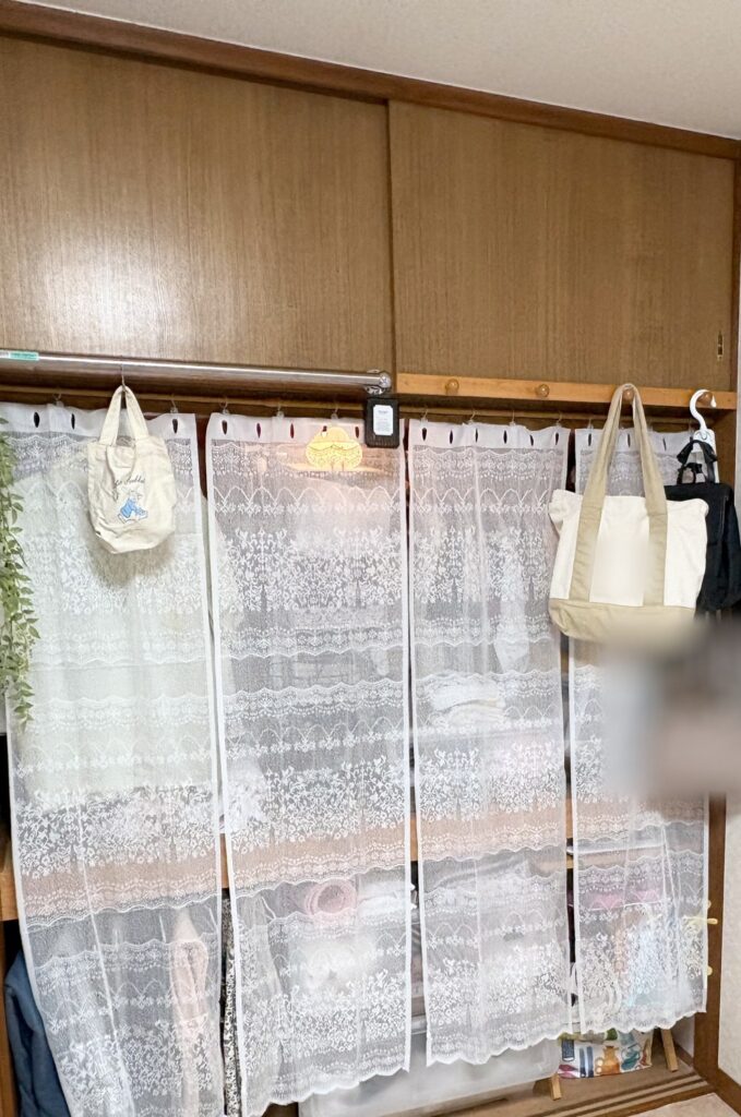 After：扉を外した押し入れに、白いレースのセパレートカーテンを4枚吊るしたところ。レース越しに中の服や収納ケースがうっすら見え、上の天袋は茶色のまま