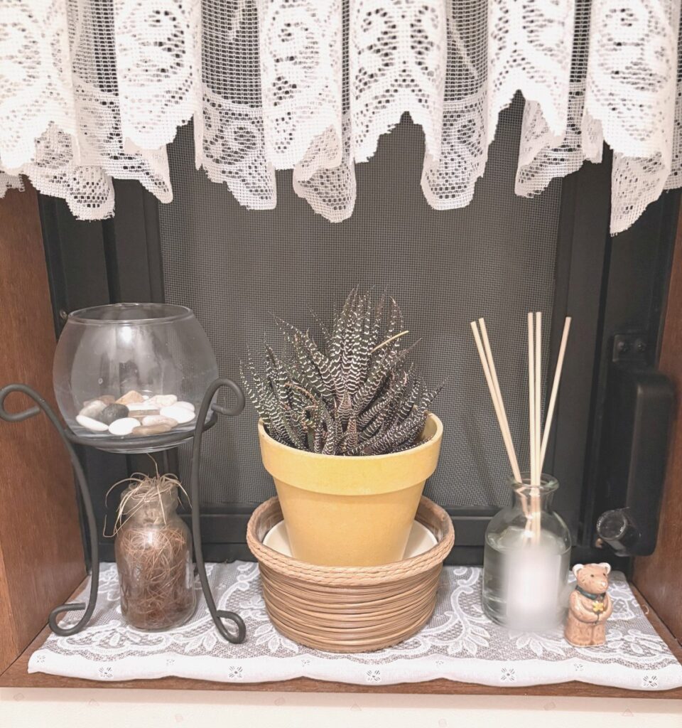 窓際の真ん中に置いた、黄色い鉢の植物。家にあった丸いかごに入れている。左にガラスの器、右にディフューザーとクマの置き物