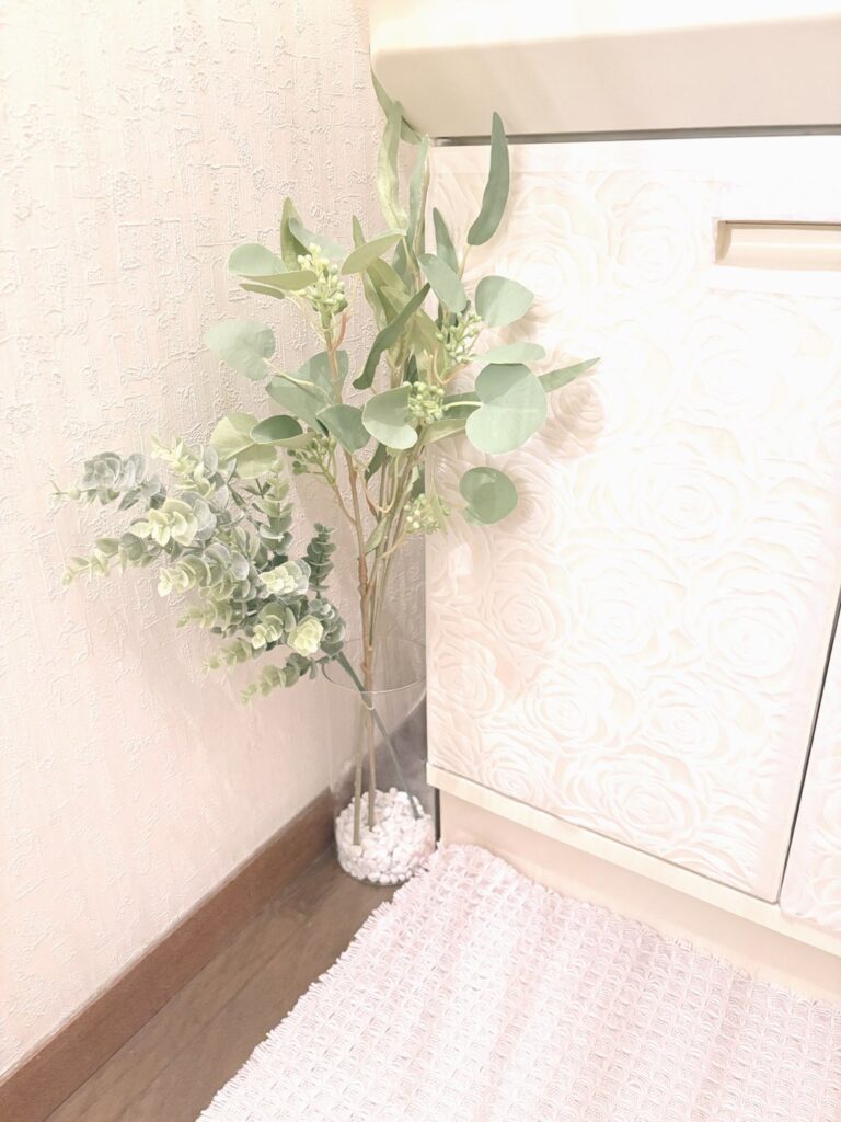 洗面台の横の床に置いた円筒形のガラス花瓶。白い砂利を入れて、ユーカリなどのグリーンを挿している