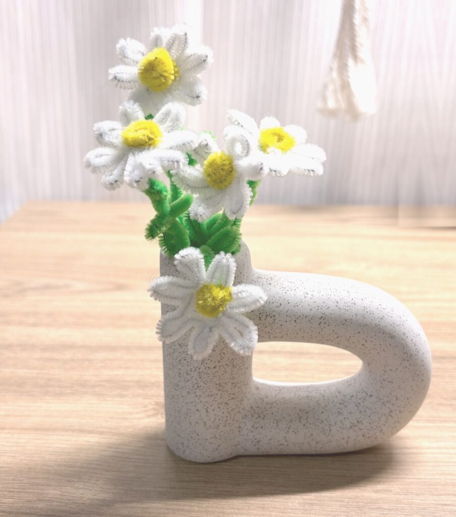 DAISOの白い花瓶に、白・黄色・緑のモールで作ったデイジーを挿して、横から見たところ