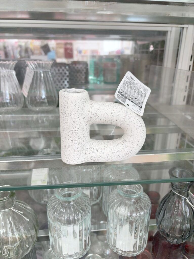 DAISOの売り場の棚に並んだ、白い陶器風の花瓶。黒い点の模様があり、横に輪っかがついた形